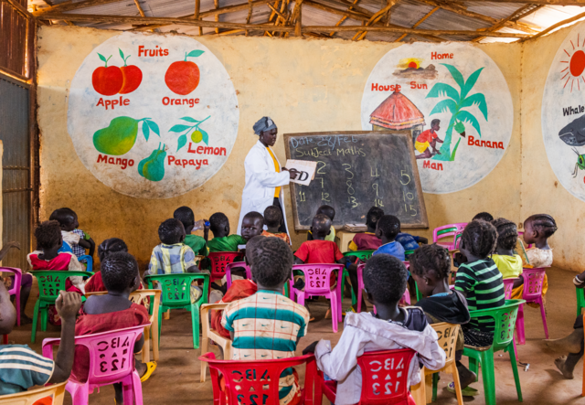 A teacher and her students in a brightly colored classroom- math is being taught.