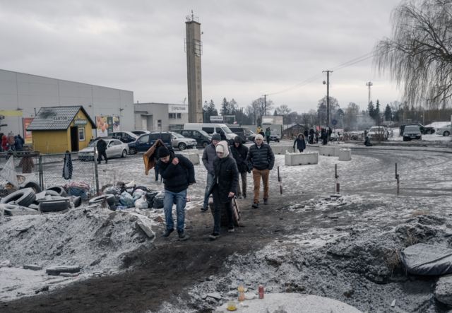 A group of refugees are walking through a cold environment, snow dots the ground.