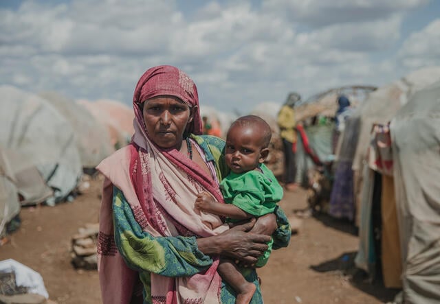 Mother stands holding her 12 month baby, in Daryel Shabellow IDP camp, Somalia.