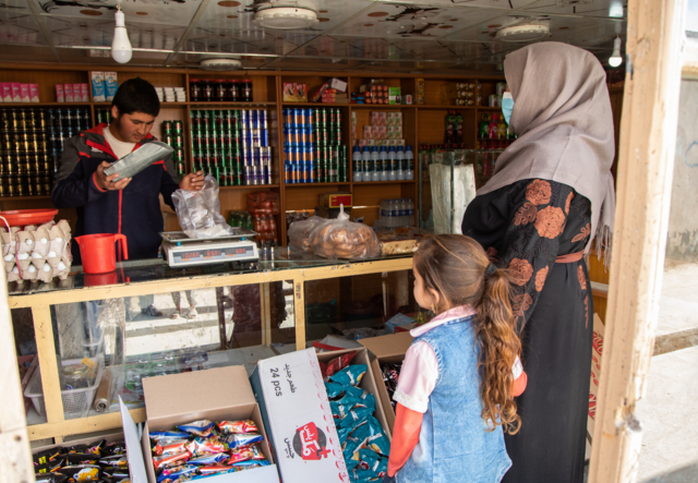 Noor holds her daughters hand while standing at a market.