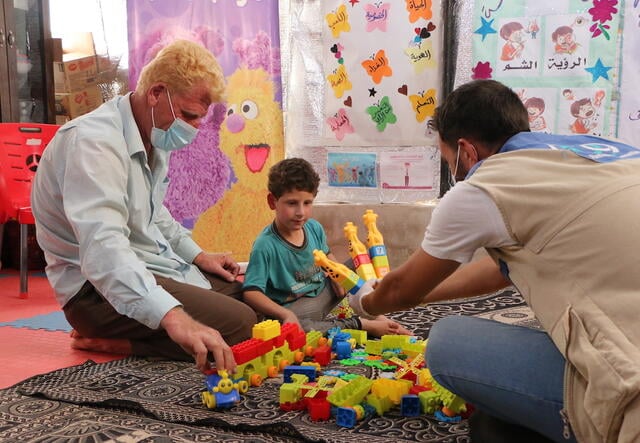 A young Syrian boy, his father, and his teacher play with educational toys on a rug.