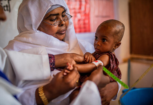 Two doctors hold young Amino. One of them gently wraps a tape around Amino's arm to measure the child's health.