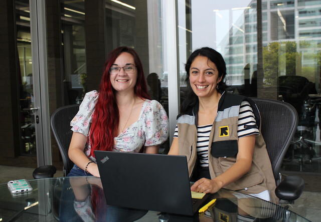 Dos mujeres se sientan frente a una computadora portátil y sonríen.