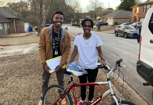 IRC Student Support Specialist, Langston Jenkins, and an adolescent male client standing with a red bike in a Clarkston neighborhood.