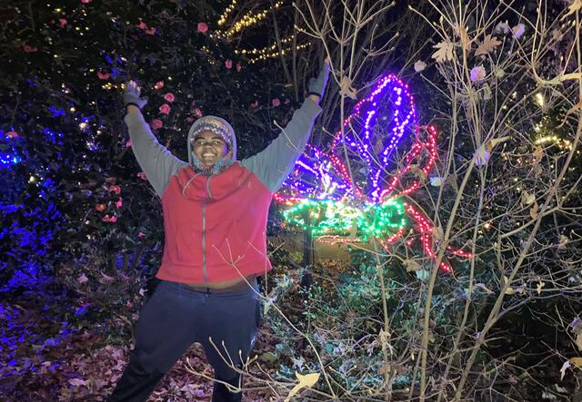 A student with his hands raised over his head in front of a light display shaped like a large flower.