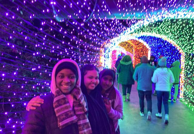 A group of 3 female students standing in a tunnel of multi-colored lights.