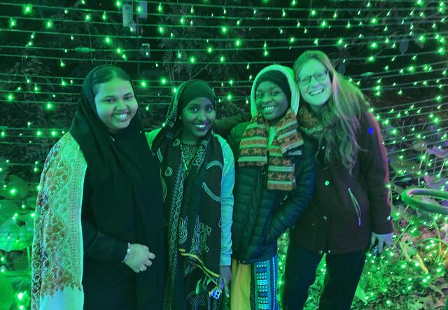 A group of 3 female students and Brynn Champney standing in front of a wall of green lights.