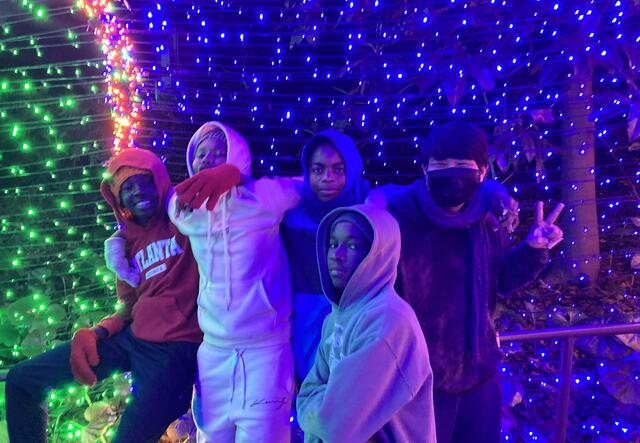 A group of four male students posed in front of a wall of green and blue lights.