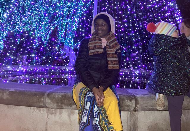 A student standing in front of a Christmas tree-like cone of blue lights.