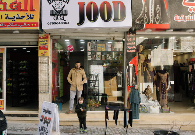 Tarek stands outside his business, Salon Jood, with his four-year-old son.