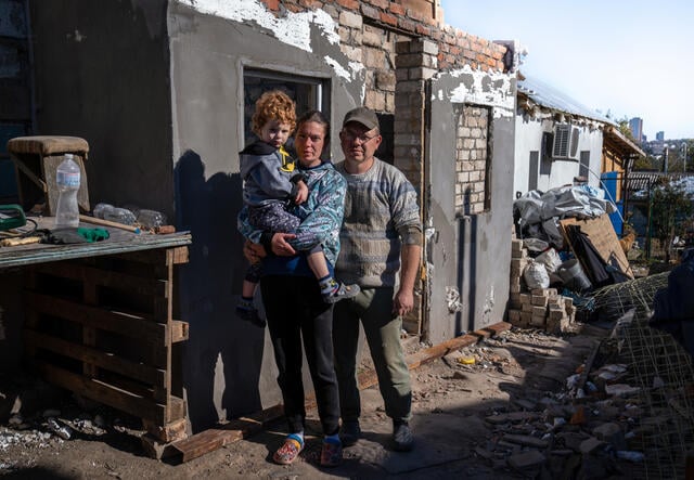 Maryna, Serhii and their family stand in front of the rubble of their home.