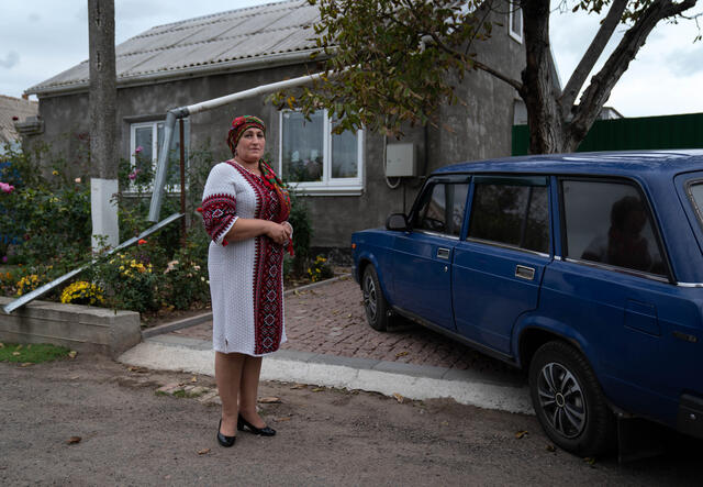 Olga stands in front of her house, facing the camera