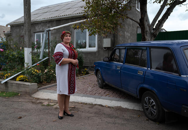 Olga stands in front of her house, facing the camera