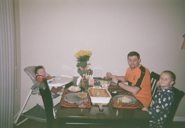 Evgen and two sons sit at dining table, ready to eat