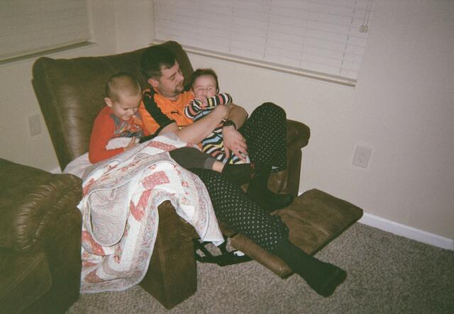 Evgen sits in an armchair with his two young children on his lap.