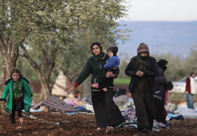 Syrians, displaced as a result of the deadly earthquake that hit Turkey and Syria on February 6, walk in an open field.
