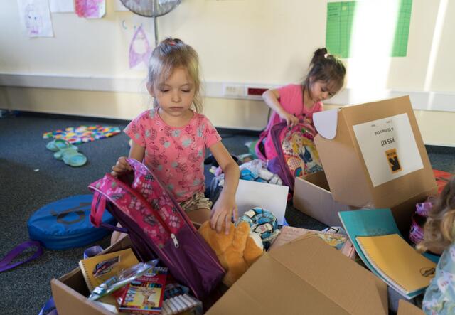 Two children each opening a box of toys and removing a backpack 