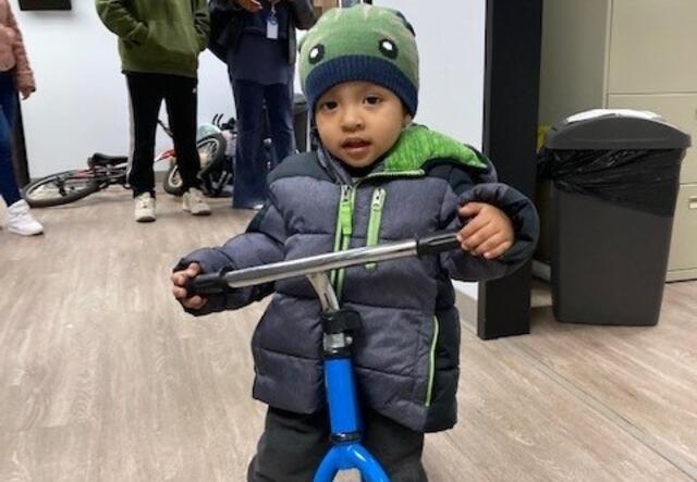 A toddler rides a blue bike in the IRC Atlanta office.