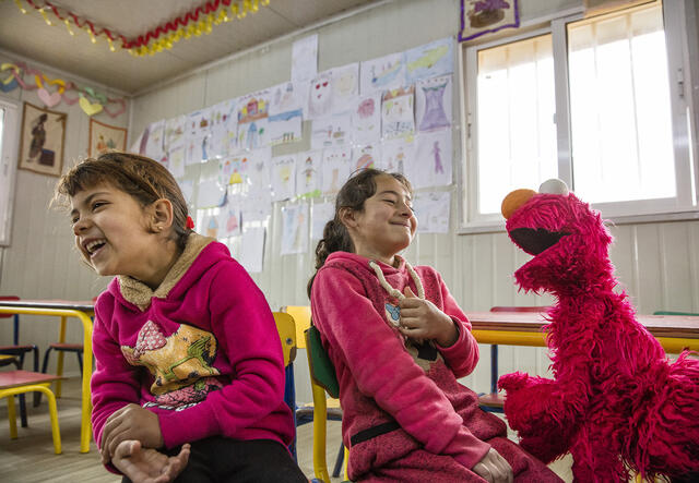 Two girls laugh with Elmo at a Ahlan Simsim location.