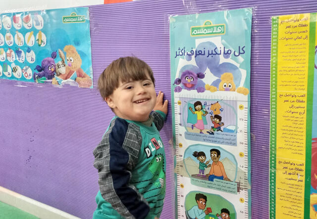Saeed stands, smiling, at an Ahlan Simsim workshop. The walls behind him are decorated with characters from the TV show.
