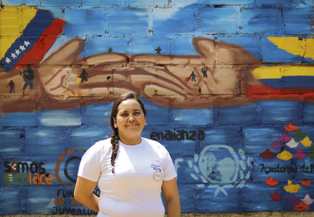 Omaira faces the camera, stood against a colorful painted wall.