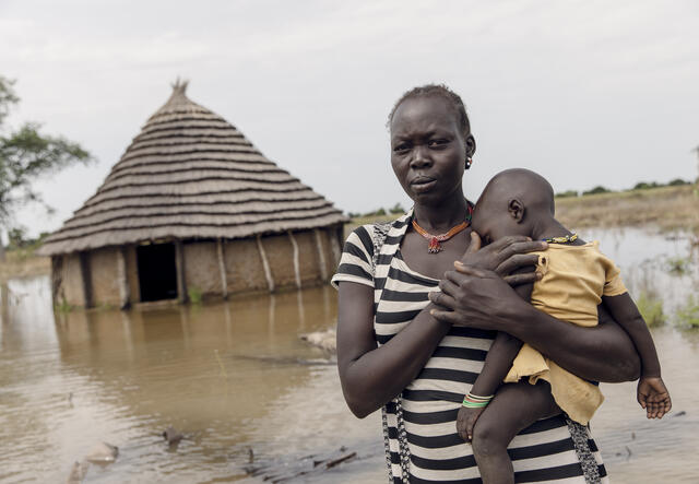 Abuk holds her child outside their flooded home in South Sudan.