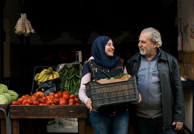 A man and a woman standing in front of a display of vegetables