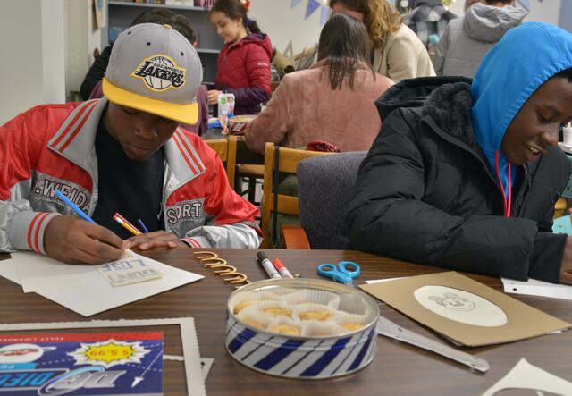 Two students sit at a desk working on their art projects. 