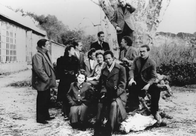 A group of artists pose for a photo outside of Villa Air-Bel. The group is smiling and one artists has climbed into a tree.