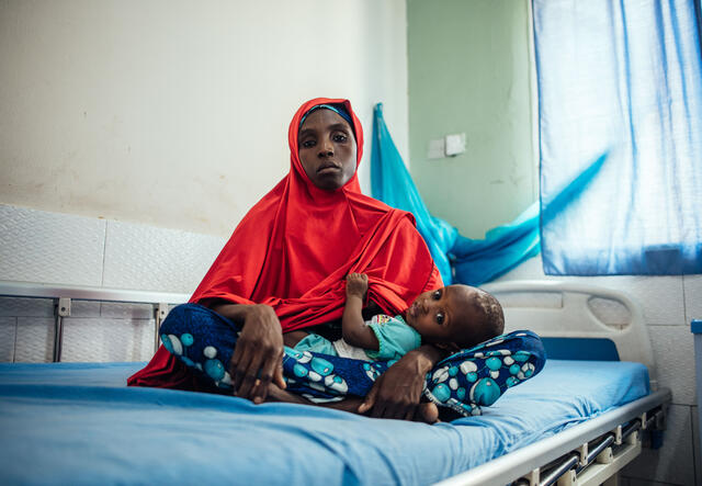 Hasfat holds her son while sitting on a bed at a medical facility in Nigeria.