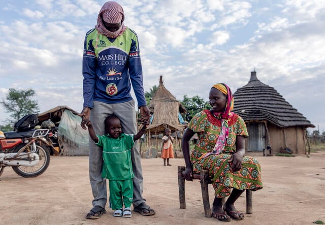 Peter stands next to his mother and father outside of their home in South Sudan.