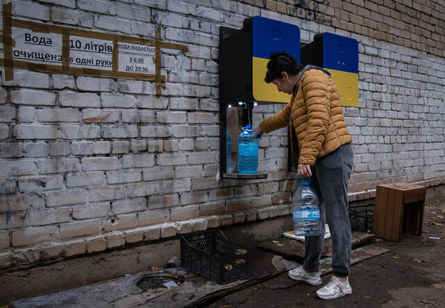 A woman fills up two big plastic water containers outside of a building in Ukraine.