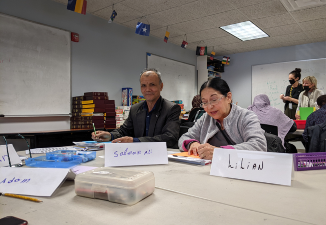 Two IRC Adult Education students studying together. In front of them are name plates reading "Salman Ali" and "Lilian."