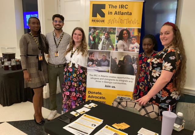 Four IRC Atlanta staff members posed for a photo, standing next to the IRC Atlanta pop-up banner.