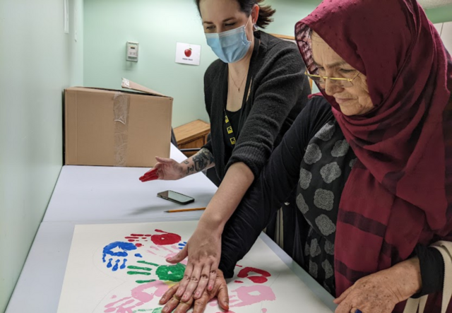 An IRC Adult Education volunteer and a student making paint handprints together.