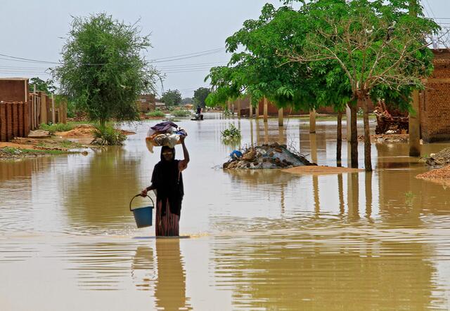 A woman wades through flood water in Managil city while carrying a basket of clothes on her head.