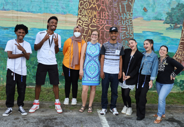 Five members of the Youth Futures graduating class of 2023 and three IRC Youth staff gathered for a group photo in front of a mural of a tree.