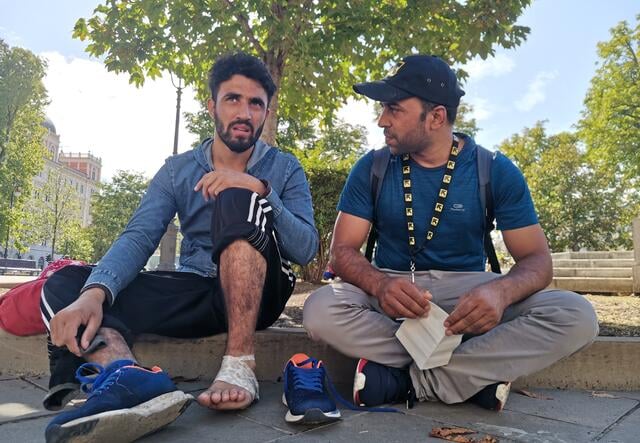 An IRC Italy staff person sits on the ground beside a newly arrived refugee to provide information
