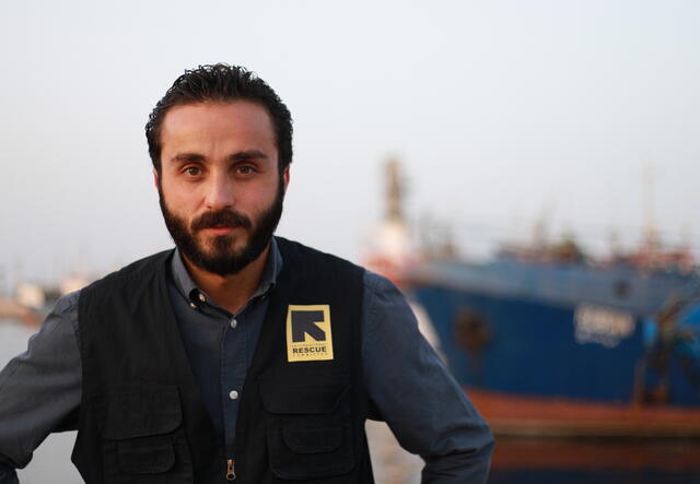 A man named, Adel wears an IRC-branded vest and faces the camera.