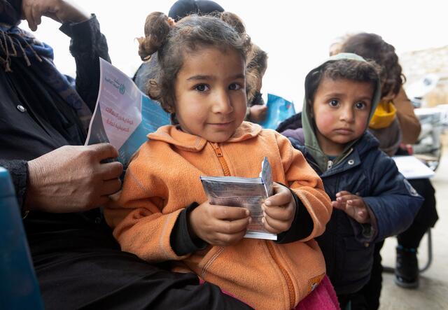 Zena* accompanied by her parents, carries rehydration salts and medicine, during an IRC cholera awareness campaign at the camp she lives in.