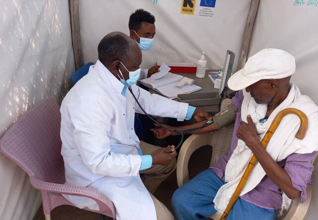 Two IRC medical staff assess the needs of an older man who sits next to them in a medical facility in Sudan.