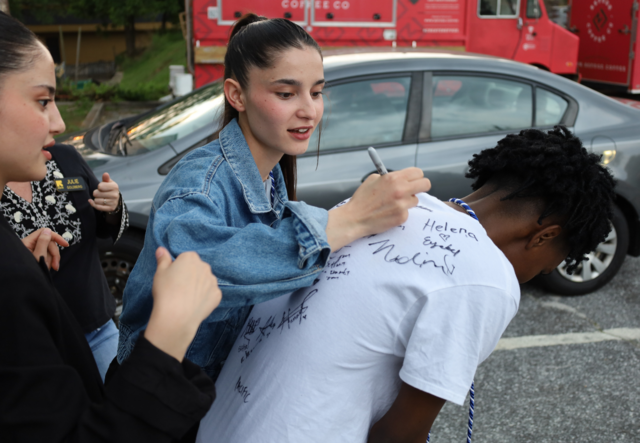 Youth Futures students in a parking lot signing the back of their classmate's white t-shirt.