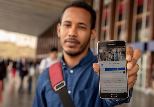 An IRC Italy client holding mobile phone showing Refugee.info resource