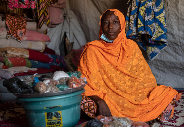 Fandaou poses for a photo in a house in Niger. Next to her is a bucket of packaged food which she sells to neighbors.