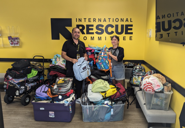 Two IRC staff standing behind a large collection of backpacks in the IRC Atlanta lobby.
