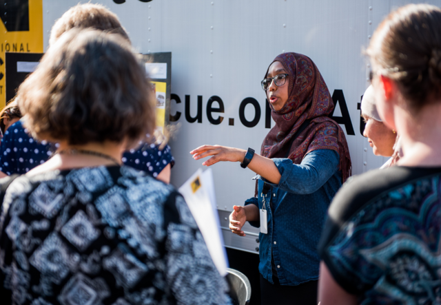 Amal Abdi speaking to a group of people while standing next to the IRC in Atlanta box truck.