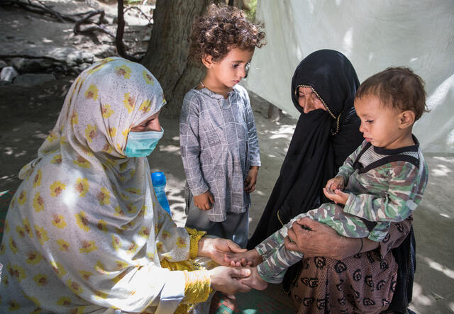 Riaz holds her youngest grandson while he is examined by IRC nutrition counselor, Marwa.