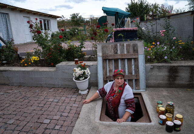 A woman steps out of an underground cellar. While the surrounding neighborhood appears peaceful, it lies near the contact lines of the war in Ukraine.
