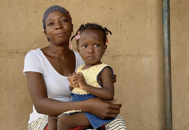 A mother sits on a chair while holding her child. Both mother and child pose for a portrait.