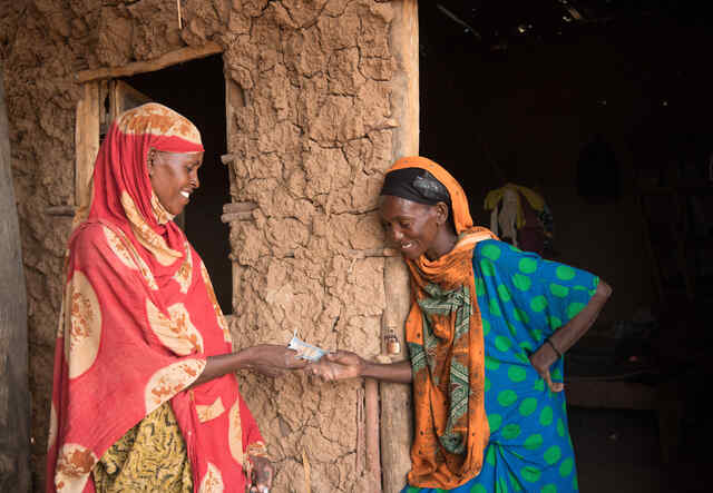 Två kvinnor fördelar RESCUE:s kontantstöd i en by i Kenya, de står framför sitt hus. 